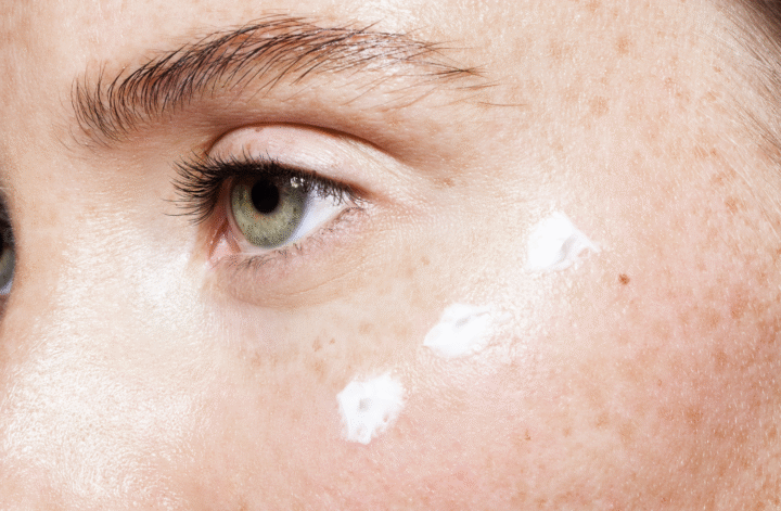 Nahaufnahme eines ungeschminkten Gesichts mit grünen Augen und punktuell aufgetragener Creme unter dem Auge – passend zum Thema „Ist Augencreme sinnvoll?“ im Kontext minimalistischer Hautpflege.